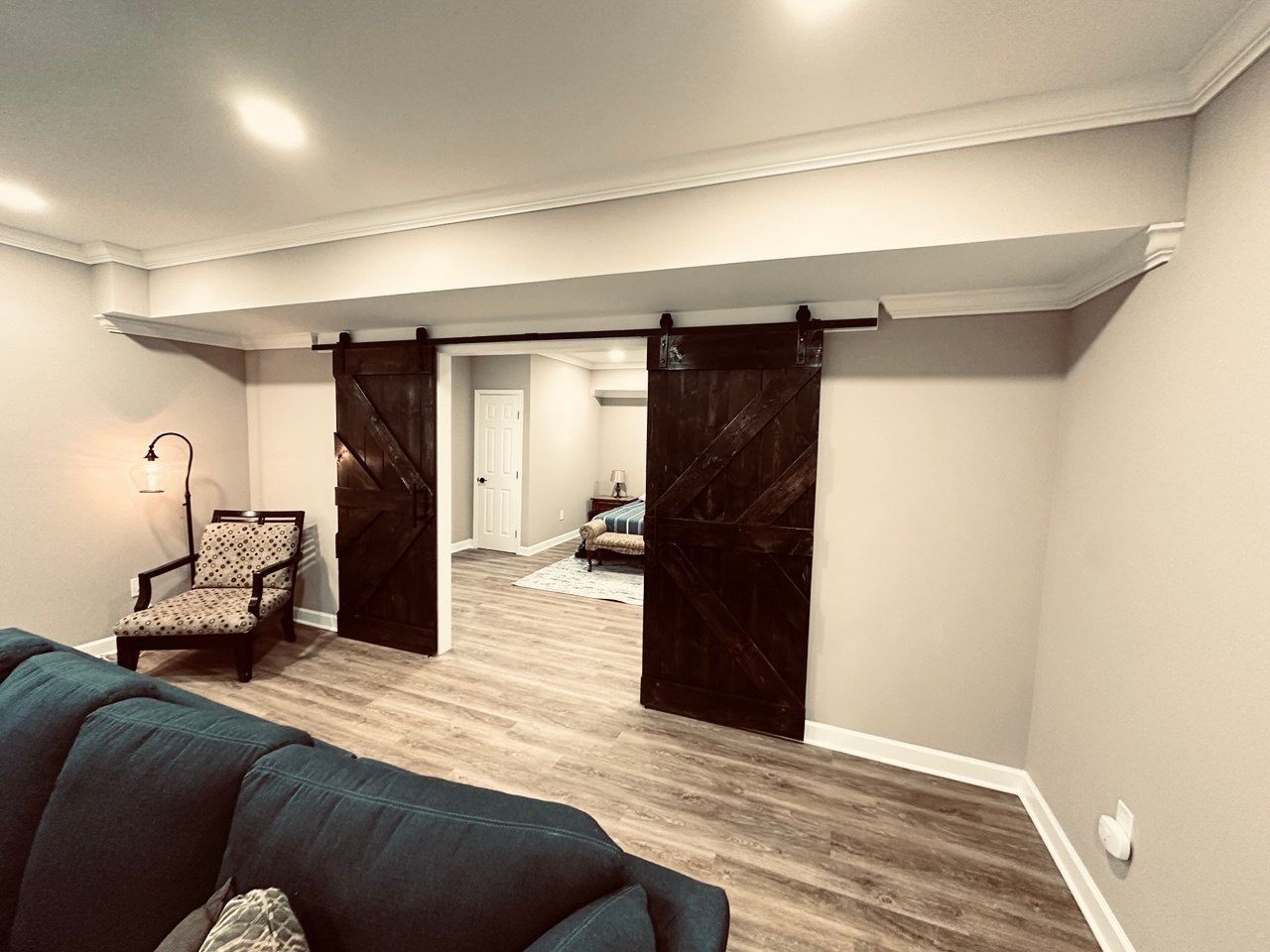 Finished basement in Finksburg with LVP flooring, wood barn door, bedroom, bathroom, gym, game area, living space, crown molding, and home theater room