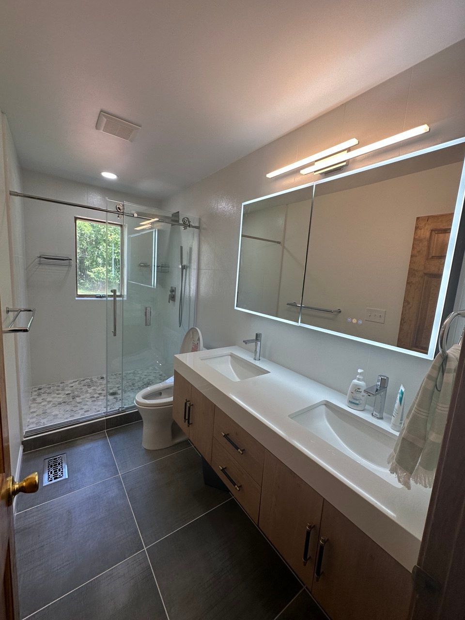 Modern bathroom remodel featuring a glass walk-in shower with tiled walls and a double vanity with quartz countertop and black fixtures.in Hunt Valley, MD