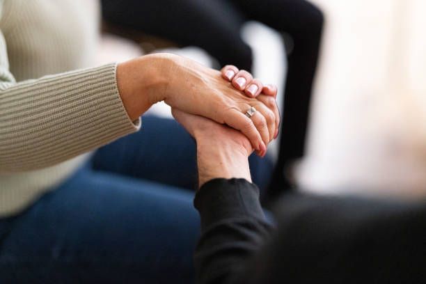 A woman is holding another woman 's hand while sitting on a couch.