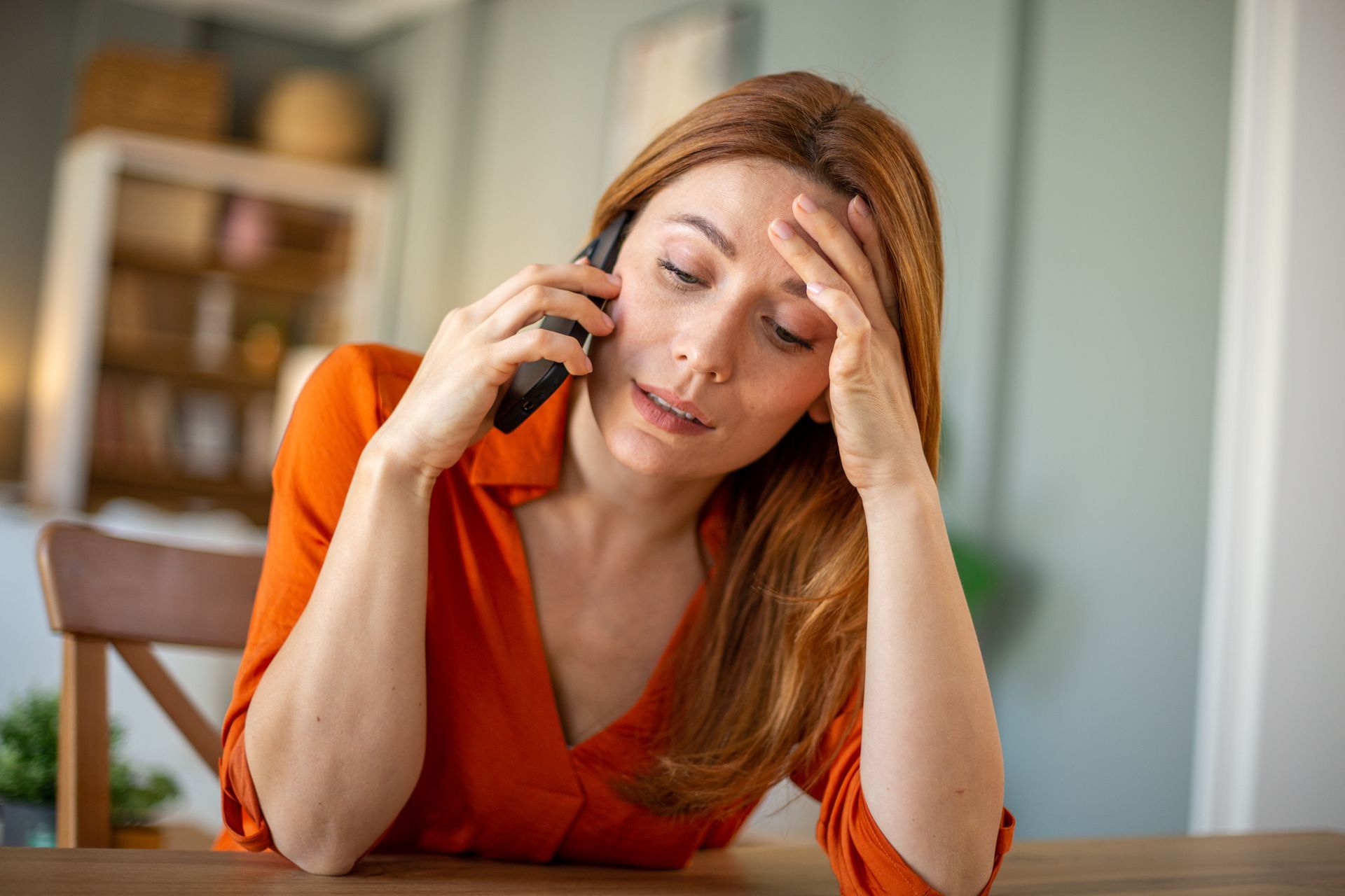 A woman is sitting at a table talking on a cell phone. A woman is sitting at a table talking on a cell phone.