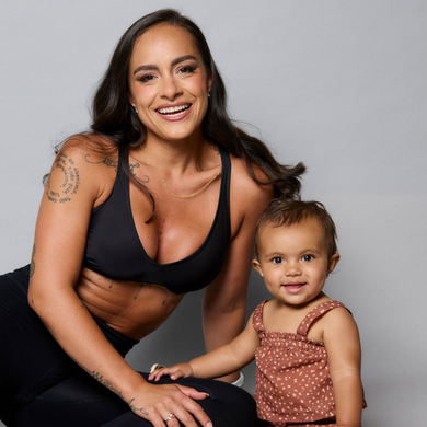 Smiling woman kneels beside a toddler in a studio portrait on a gray background