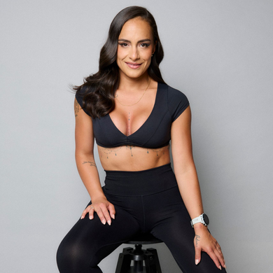 Woman sitting on a stool in black workout clothes against a gray background