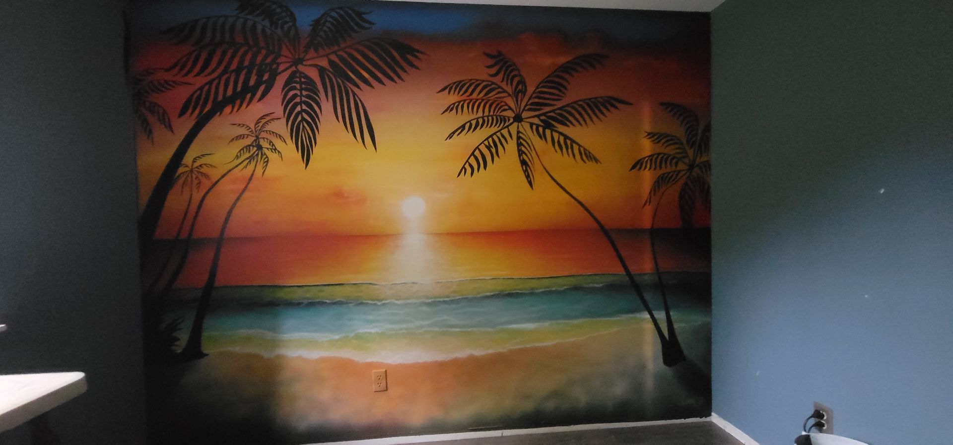 Hand-painted sunset beach mural with palm trees and ocean waves on a wall