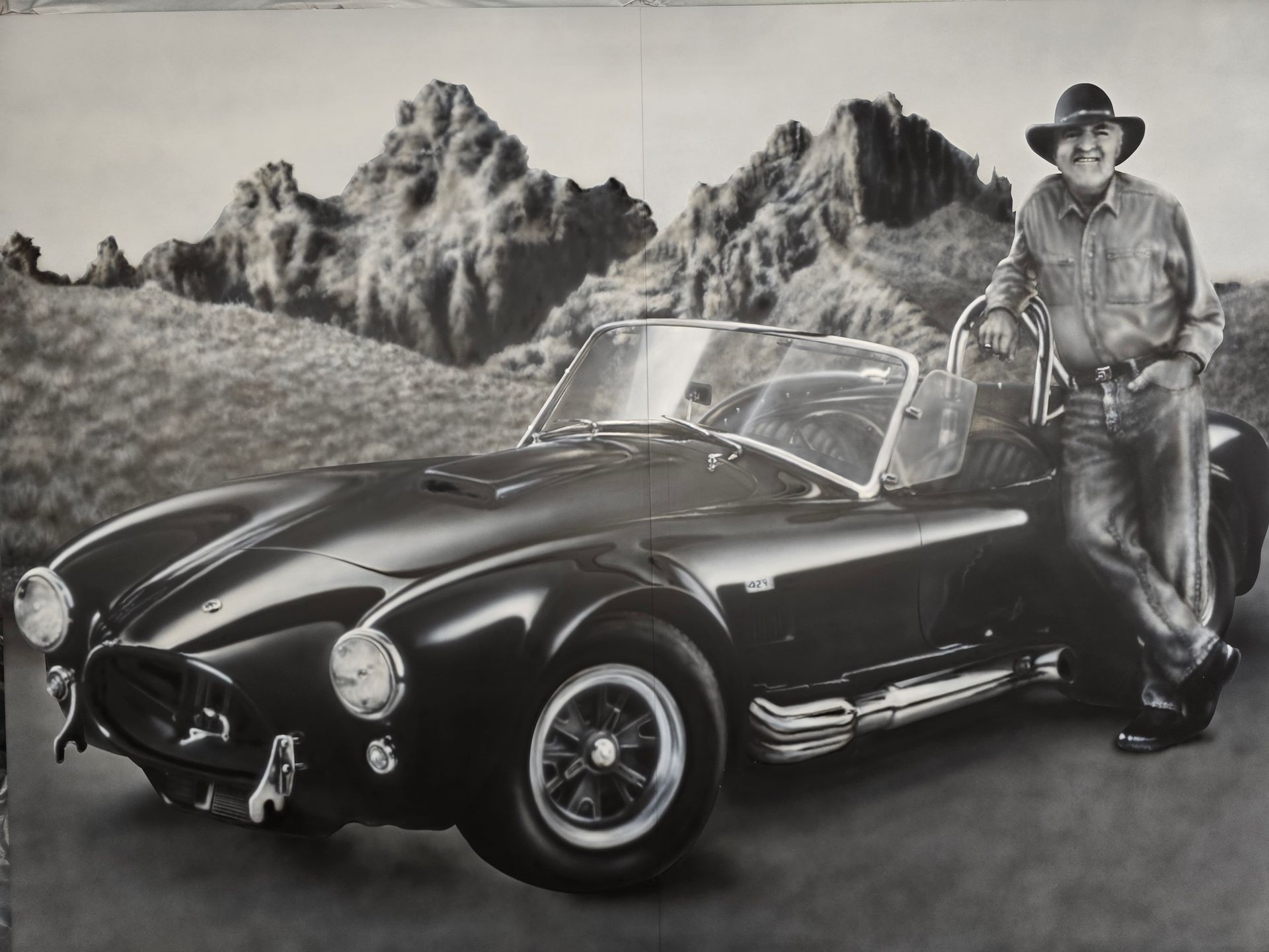 Classic black sports car with a cowboy leaning against it in front of a rocky desert backdrop