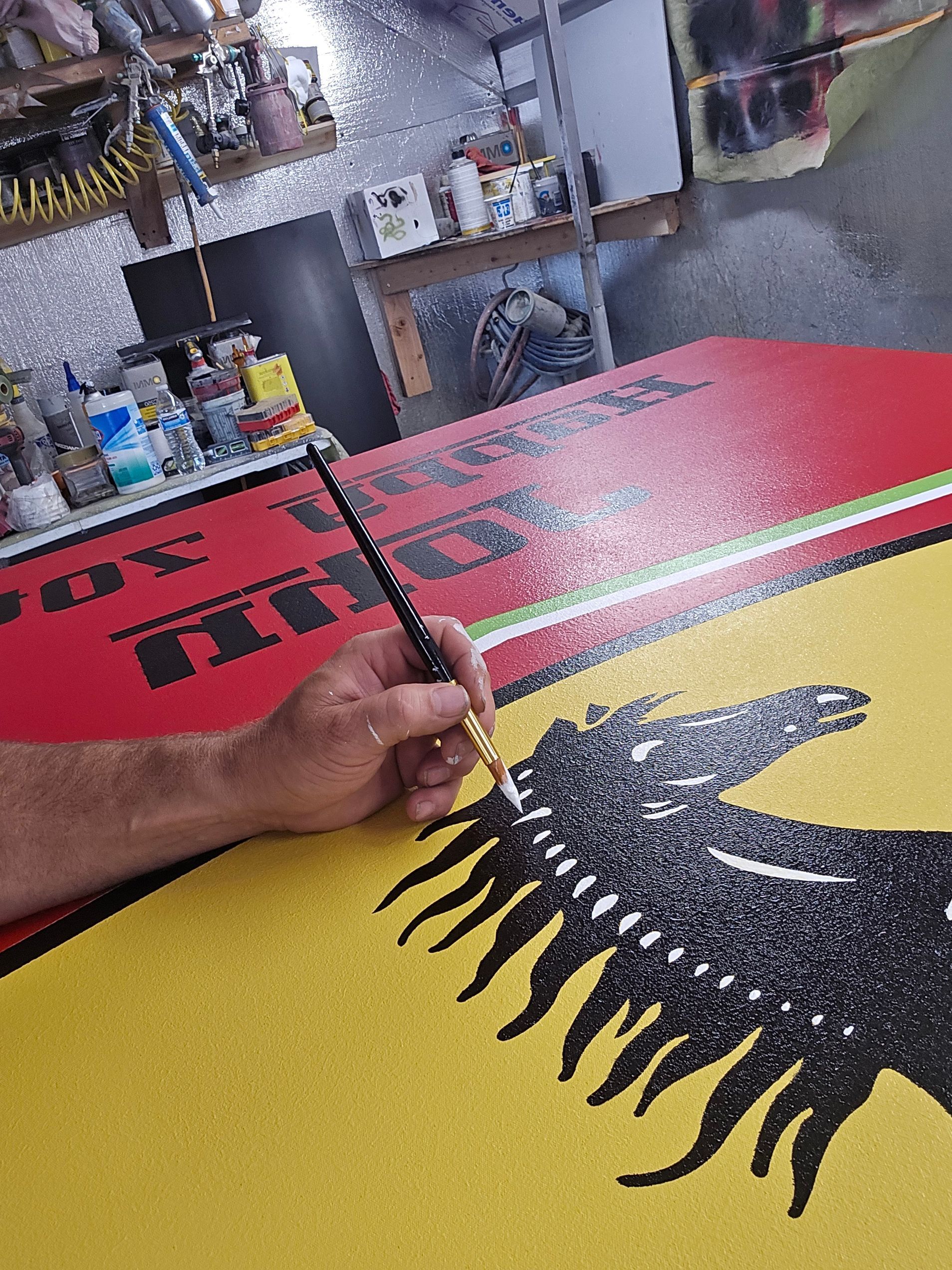 Hand painting a black sunburst on a red-and-yellow sign in a workshop
