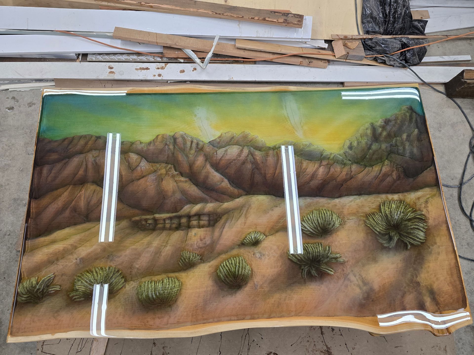 Landscape painting of mountains, desert shrubs, and a green-yellow sky