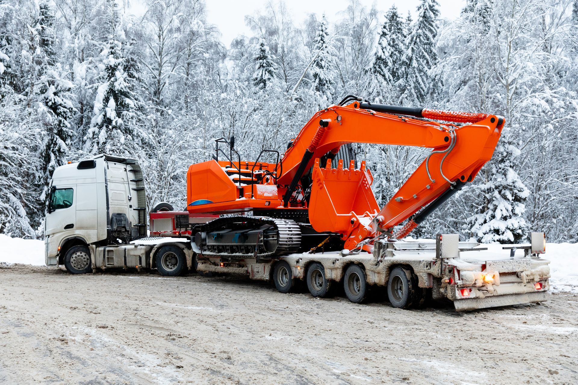 Side view tow truck with excavator parked in winter on snowy trees background. Side view tow truck with excavator parked in winter on snowy trees background.