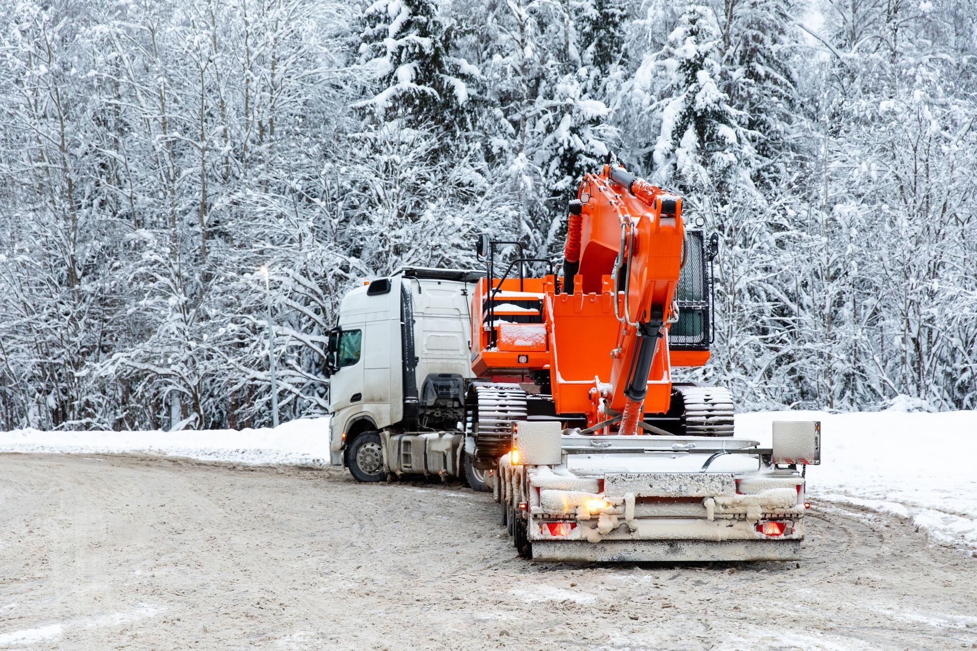 Rear view tow truck with excavator parked in winter on snowy trees background Rear view tow truck with excavator parked in winter on snowy trees background