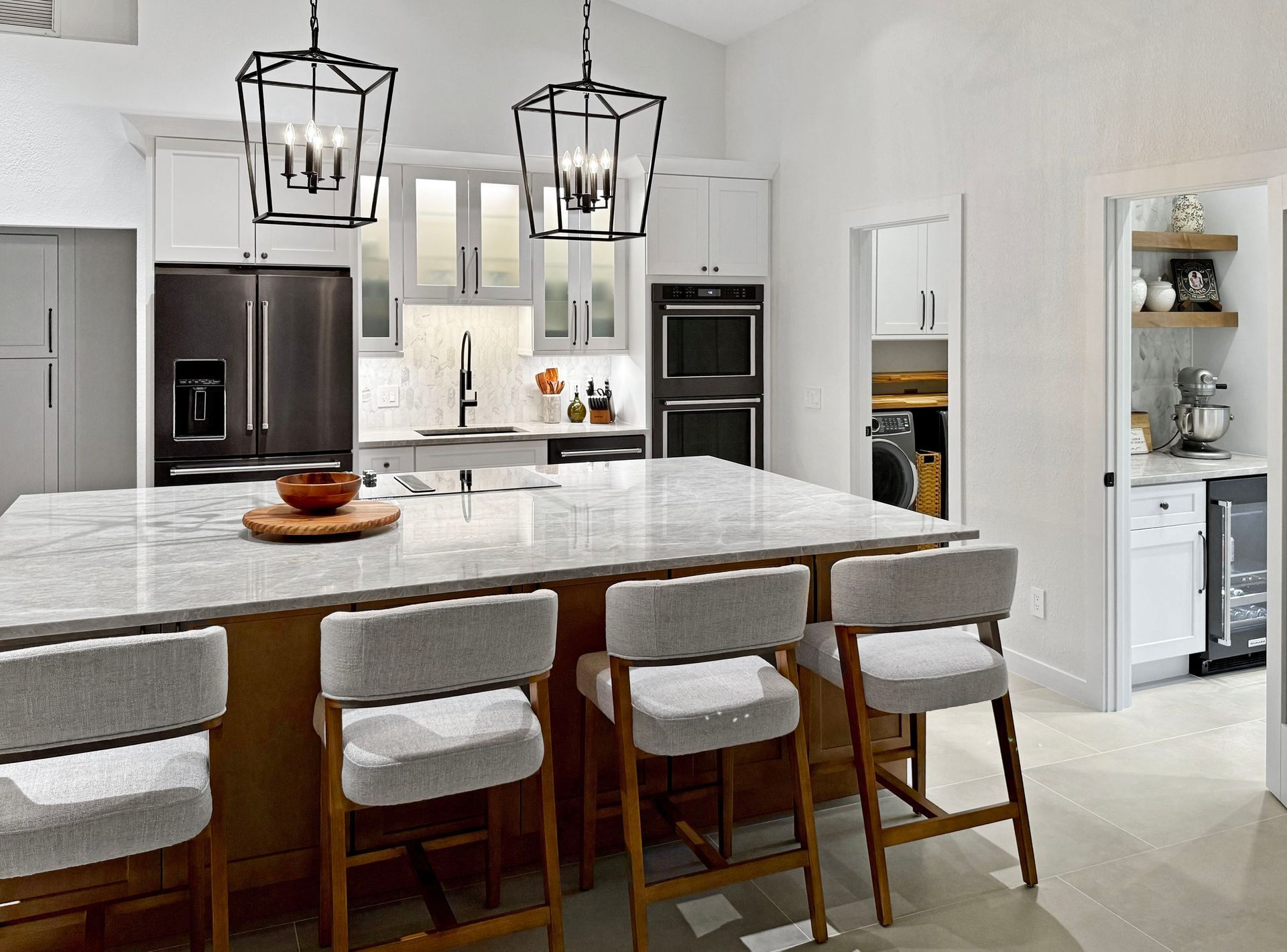 Modern kitchen with island seating and pendant lights. Stainless steel appliances, white cabinets, and light countertops.