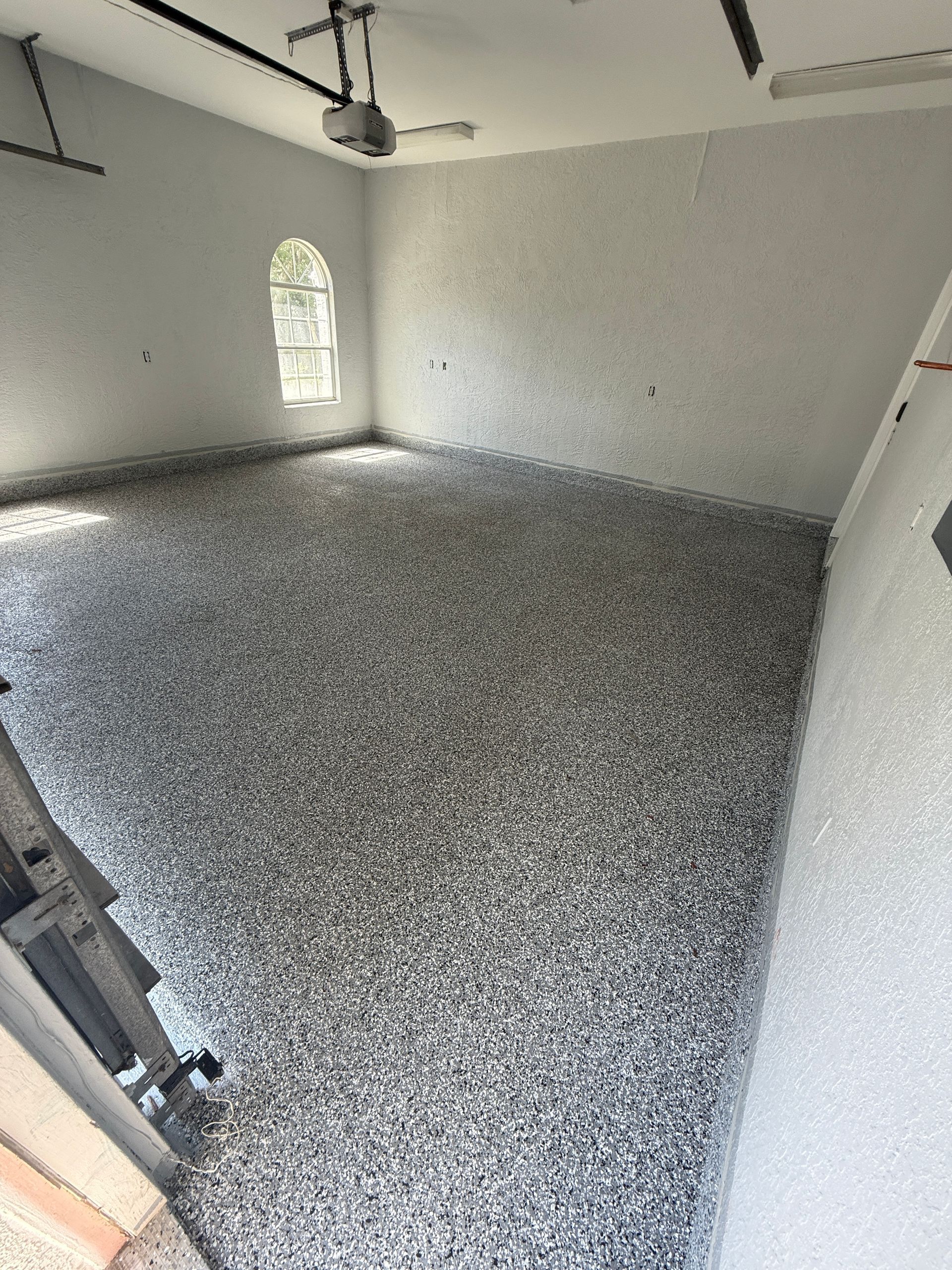 Empty room with speckled, gray flooring and white walls. Arched window.