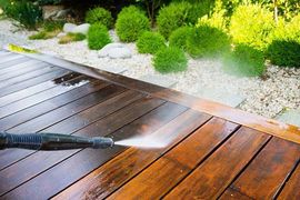 Pressure washing a wooden deck, spraying water.