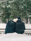 Deux personnes en manteaux d'hiver sont assises sur des sentiers enneigés, leurs têtes se touchant
