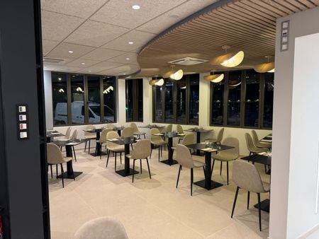 Intérieur du restaurant : tables et chaises, plafond incurvé avec éclairage, fenêtres avec vue sur la ville.
