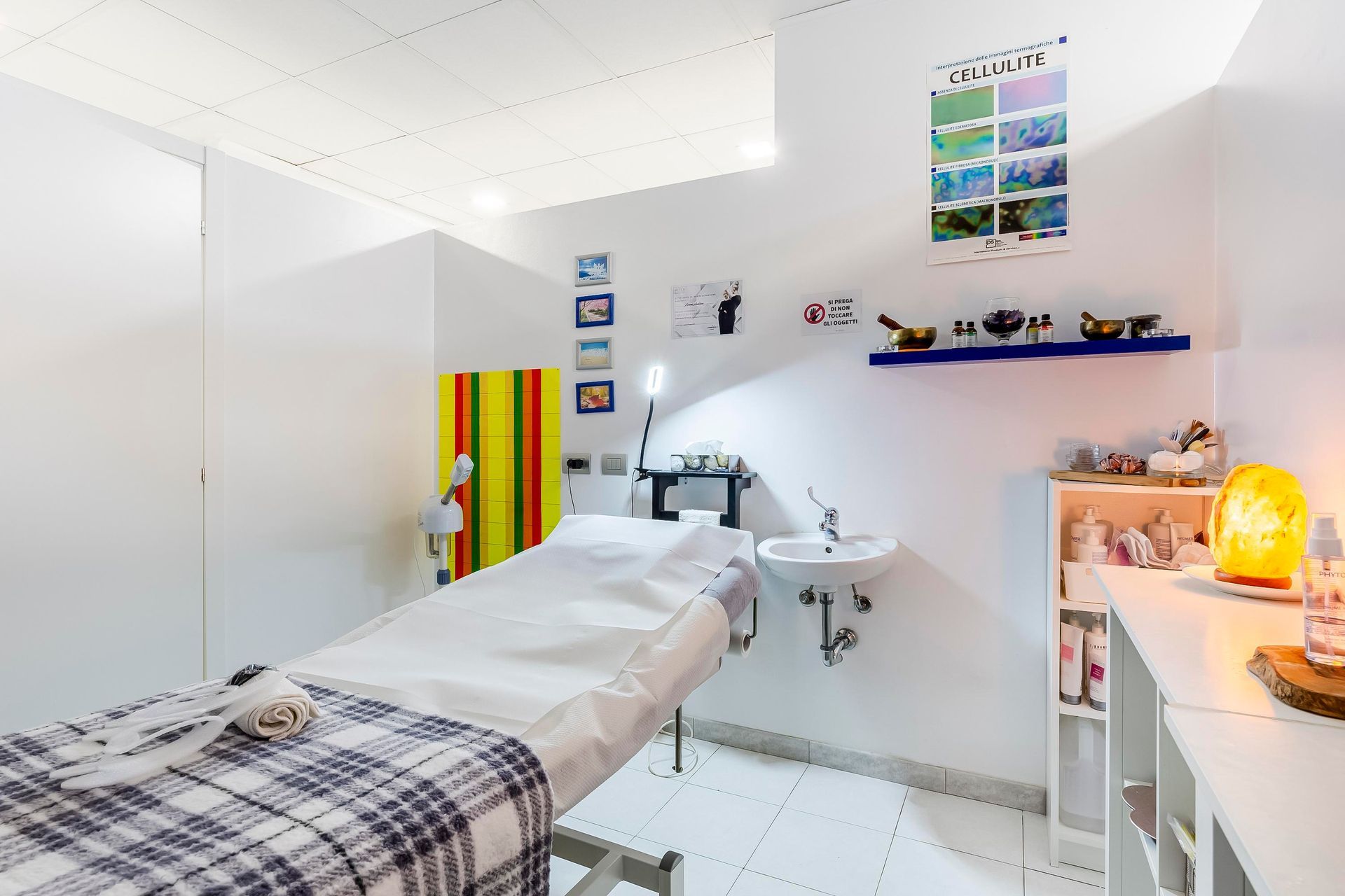 Luminosa sala per trattamenti spa con lettino da massaggio, mensole, lavandino e decorazioni colorate.