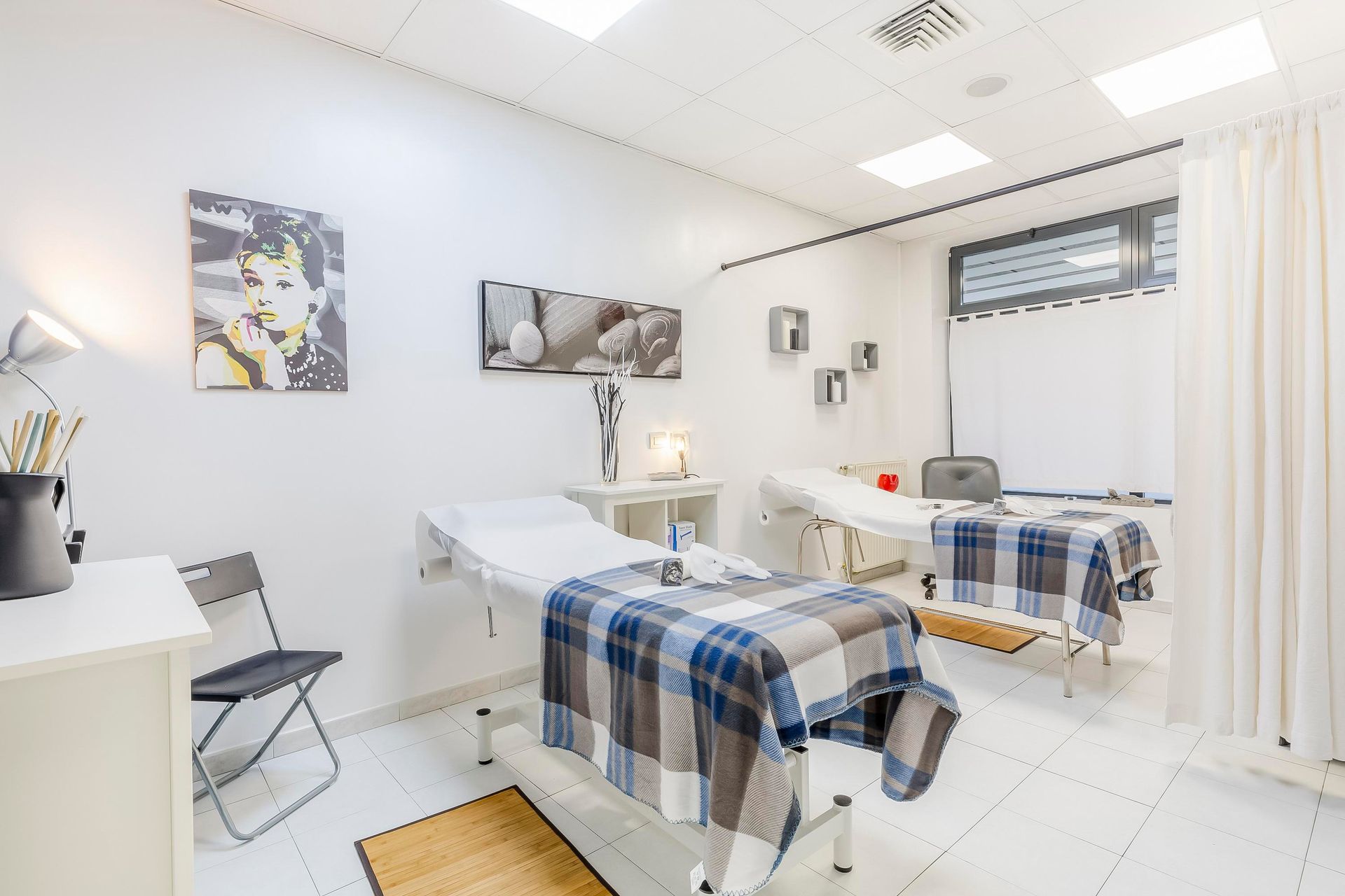 Luminosa stanza clinica con due lettini per trattamenti coperti, pareti bianche e illuminazione soffusa.