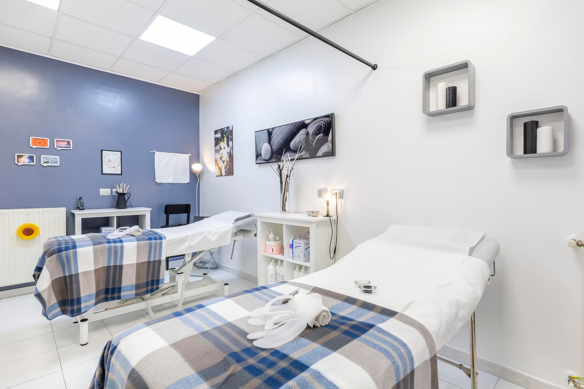 Luminosa sala per visite mediche con due letti, coperte a quadri blu e apparecchiature mediche a parete.