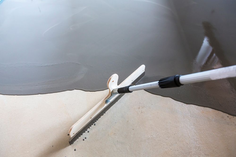 A Squeegee Spreads Gray, Self-leveling Compound Across a Floor Surface — Hobart Tiling Solutions In Clarendon Vale, TAS