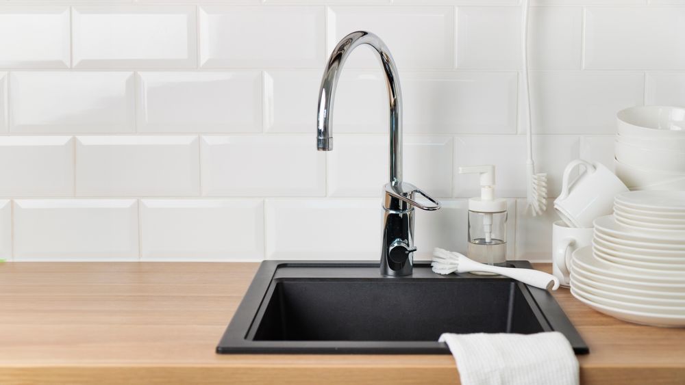 A chrome kitchen faucet stands over a black sink set into a wood countertop against a white tiled backsplash. — Hobart Tiling Solutions In Clarendon Vale, TAS