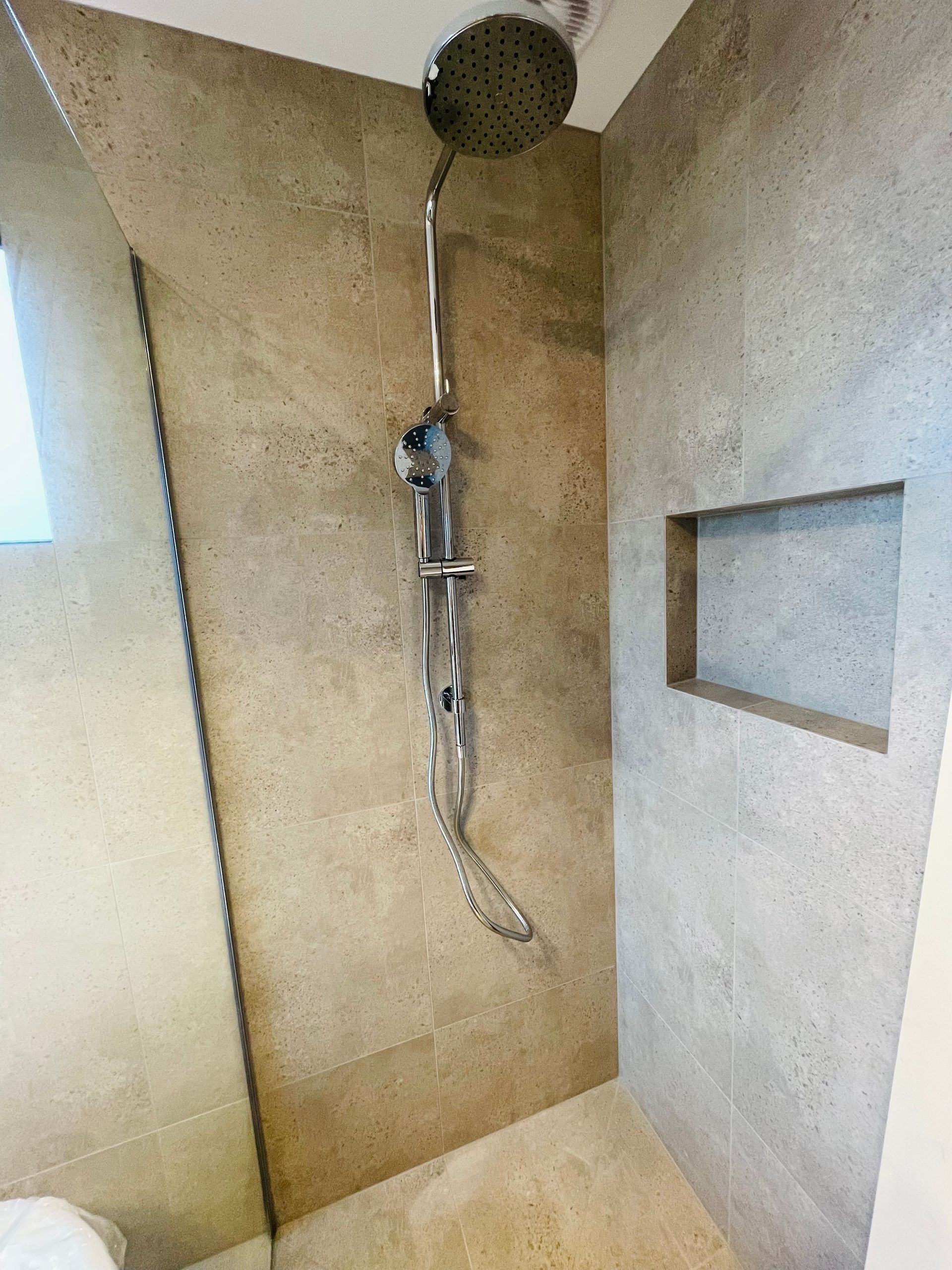 A Shower Stall With Light-brown Stone Tile Walls, a Chrome Rain Shower Head — Hobart Tiling Solutions In Clarendon Vale, TAS