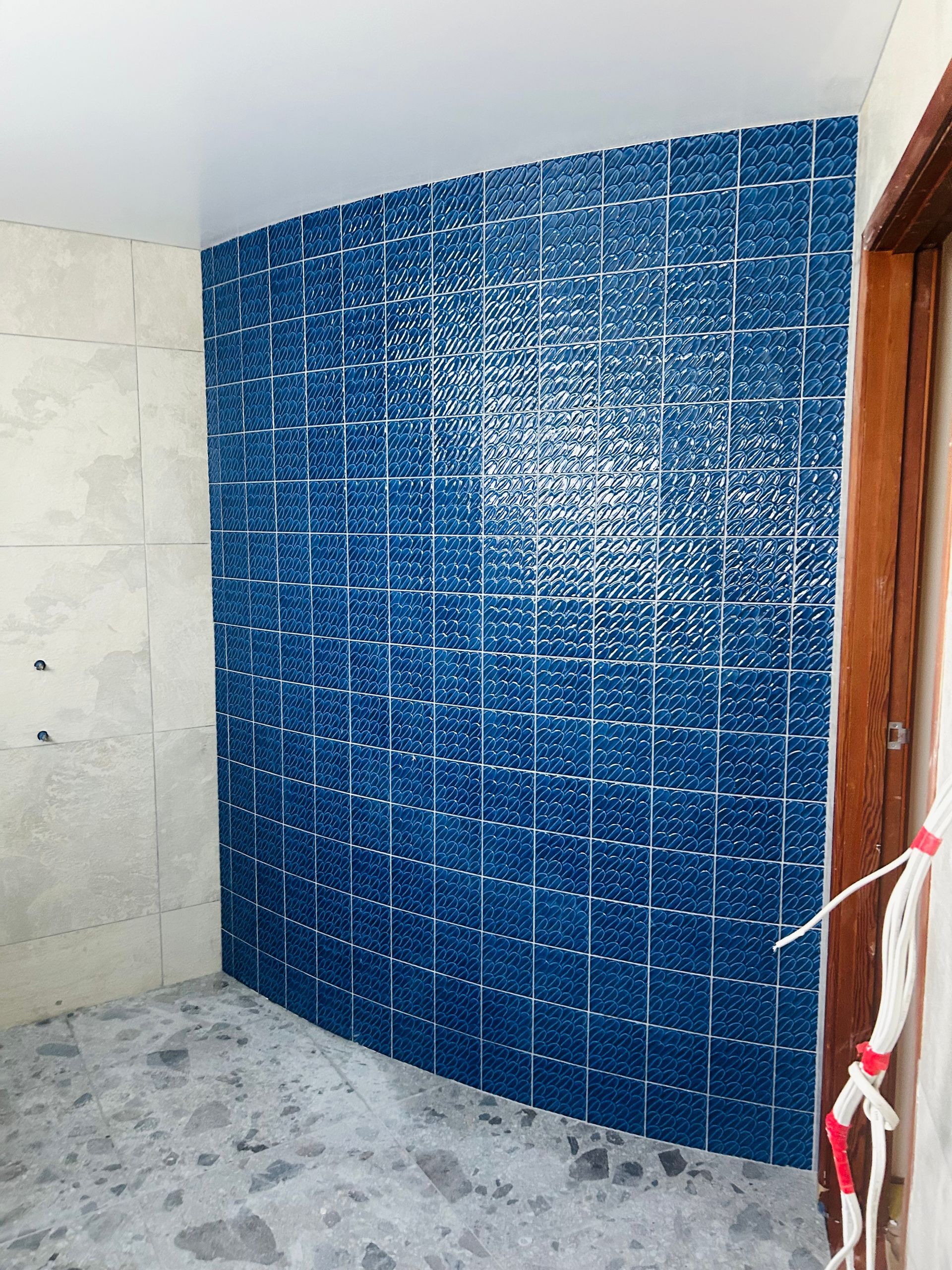 A blue tiled wall in a room under construction, with visible white grout lines and grey flooring. — Hobart Tiling Solutions In Clarendon Vale, TAS