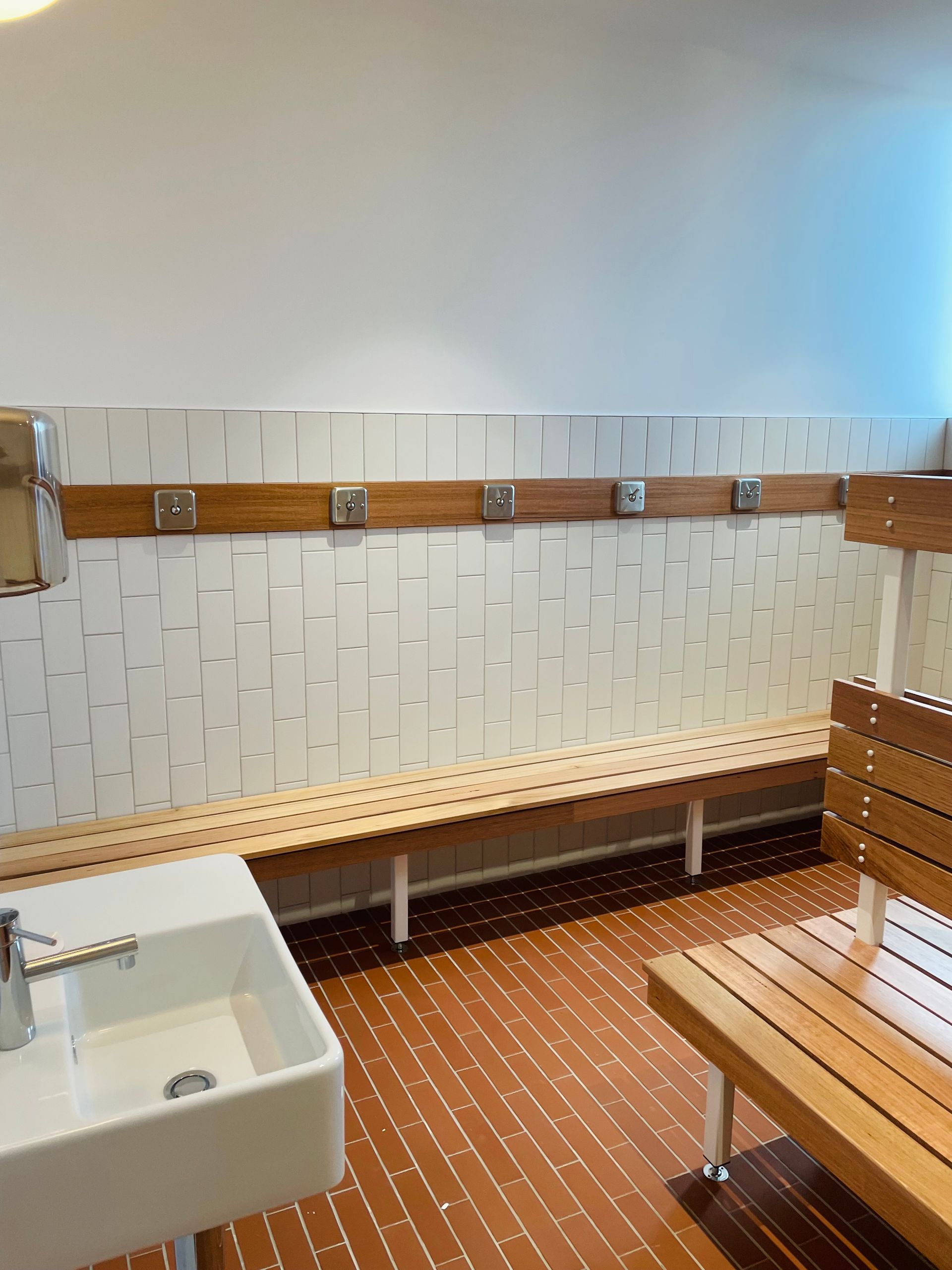 A white sink and wooden bench seating in a clean, modern locker room with tiled walls and floors. — Hobart Tiling Solutions In Clarendon Vale, TAS