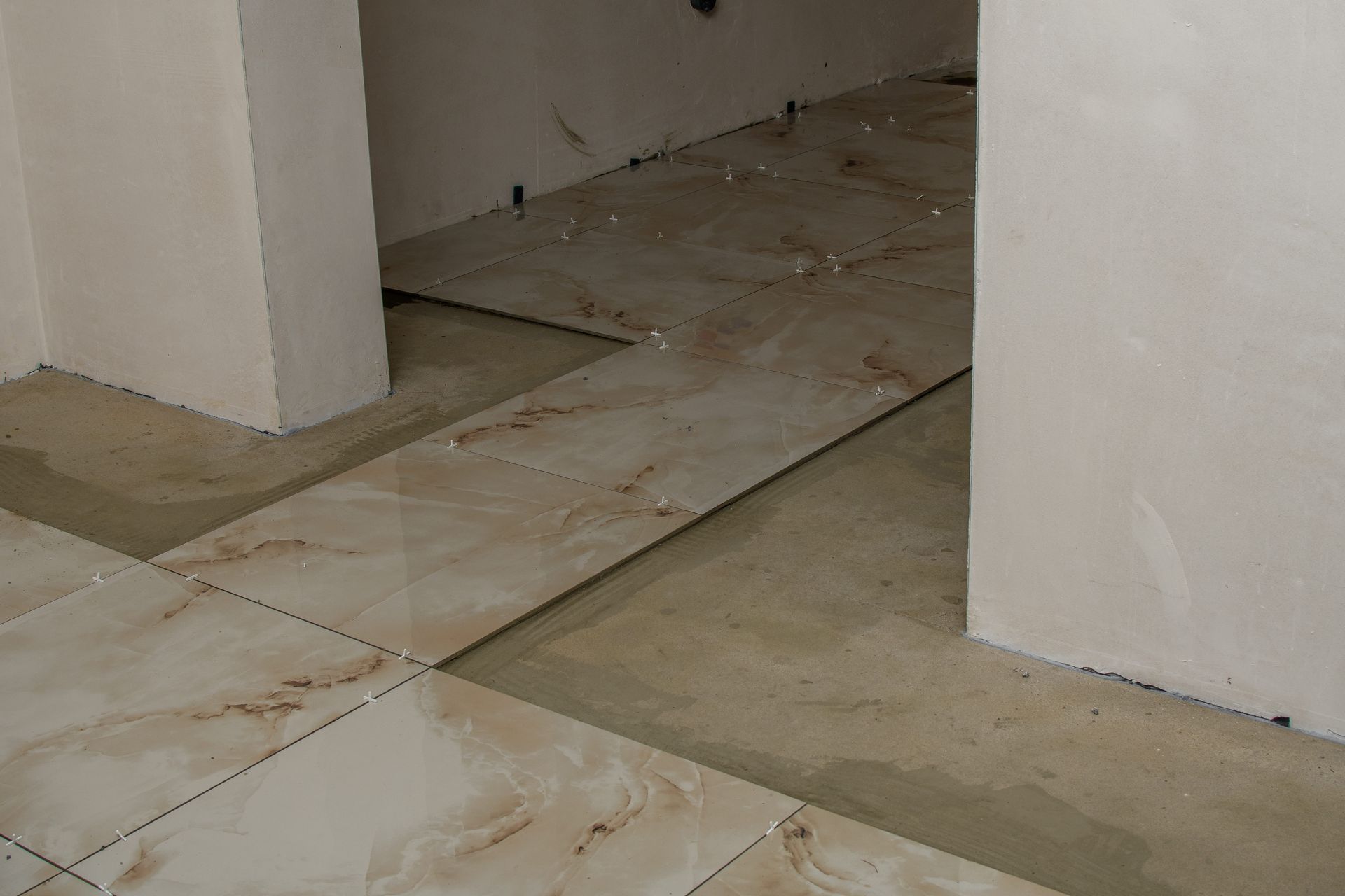 Light-colored marble-patterned tiles being laid on a concrete floor in an unfinished room — Hobart Tiling Solutions In Clarendon Vale, TAS
