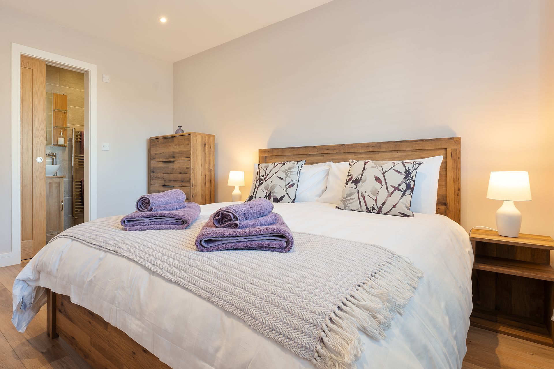 A bedroom with a king size bed , two lamps , a nightstand and a dresser.