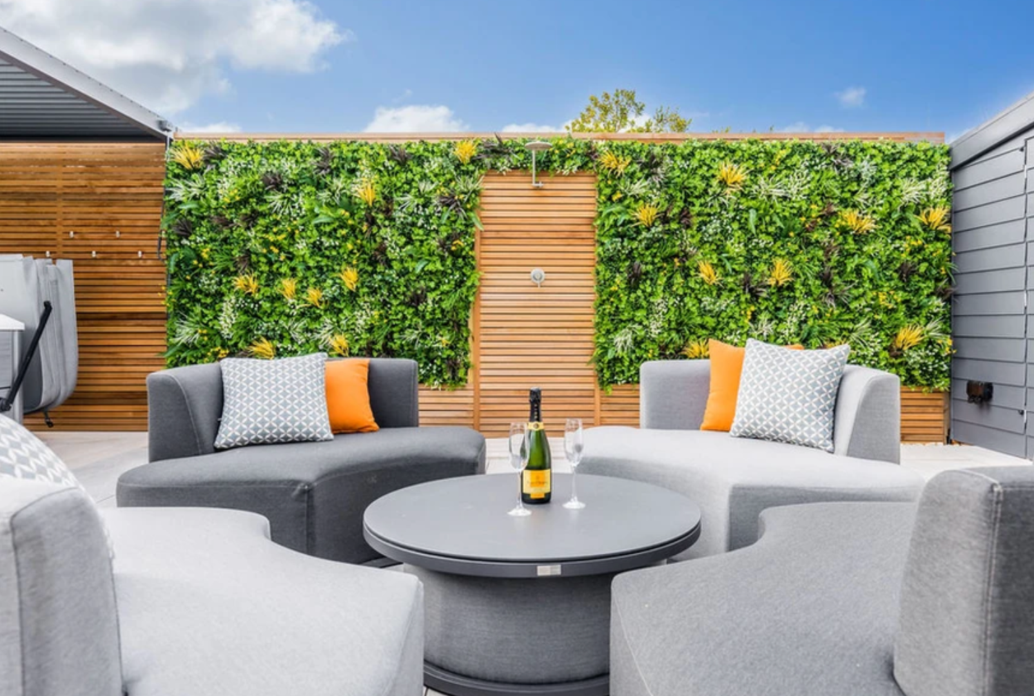 A patio with a couch , chairs and a table with a bottle of wine on it.