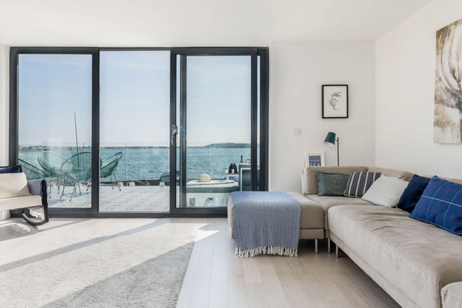 A living room with a couch , chair , ottoman and sliding glass doors overlooking the ocean.
