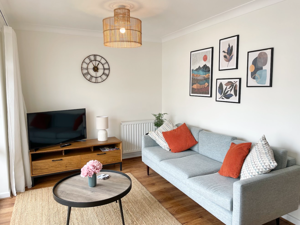A living room with a couch , table , television and a clock on the wall.