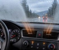 Driver’s view through a rainy windshield on a wet road with taillights ahead and dashboard controls visible