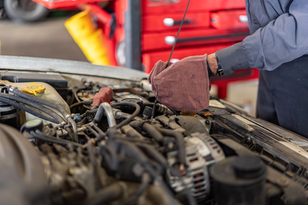 Mechanic wearing gloves working under a car hood in a garage