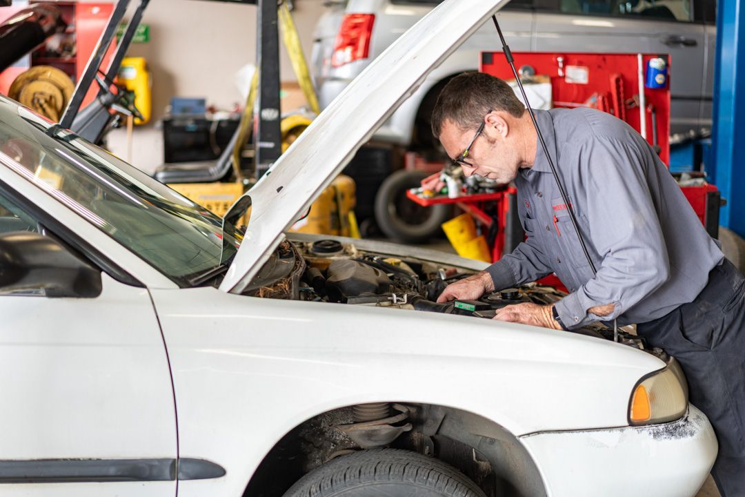 Mechanic inspecting a white car with the hood open in an auto repair shop