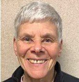 A woman with gray hair and glasses is smiling for the camera.