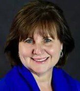 A woman wearing a blue jacket and earrings is smiling for the camera.