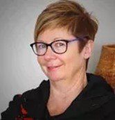 A woman wearing glasses and a black jacket is smiling for the camera.