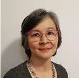 A woman wearing glasses and a necklace is smiling for the camera.