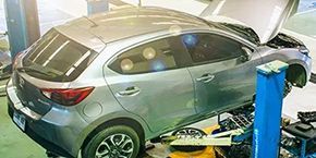 A car is sitting on a lift in a garage with its hood open.