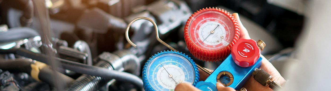 Hands hold a blue and red manifold gauge set near an engine.