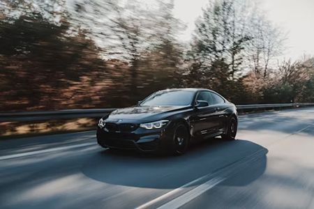Black sports car speeding on a road with blurred trees in the background.