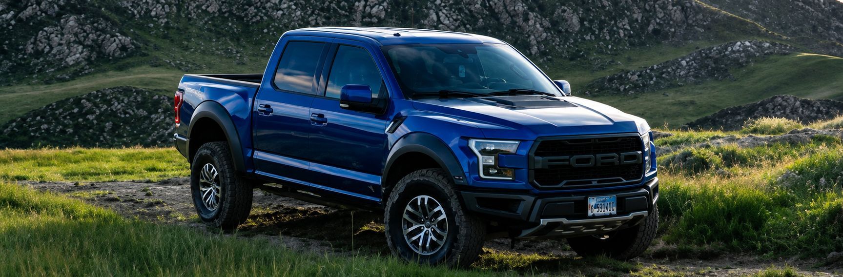 Blue pickup truck driving on a dirt road through a grassy, mountainous landscape.