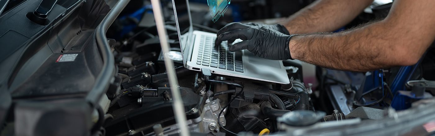 Hands wearing black gloves working on car engine, holding air filter.