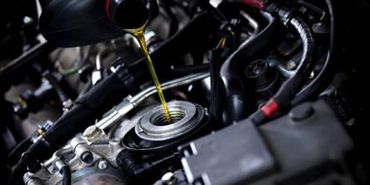 A close up of a person pouring oil into a car engine.