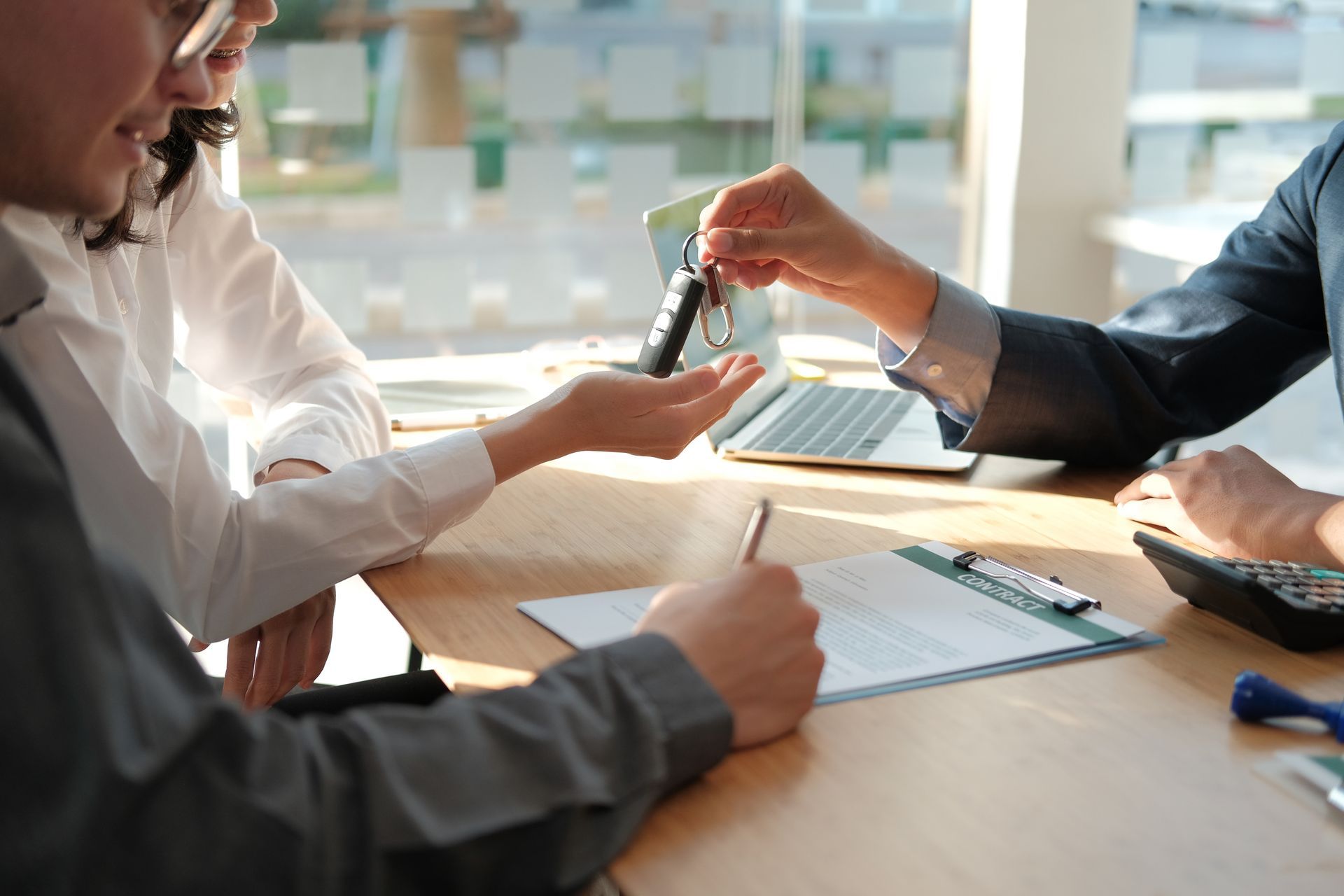 Loan officer handing car keys to a customer while financing documents are signed at a financial serv