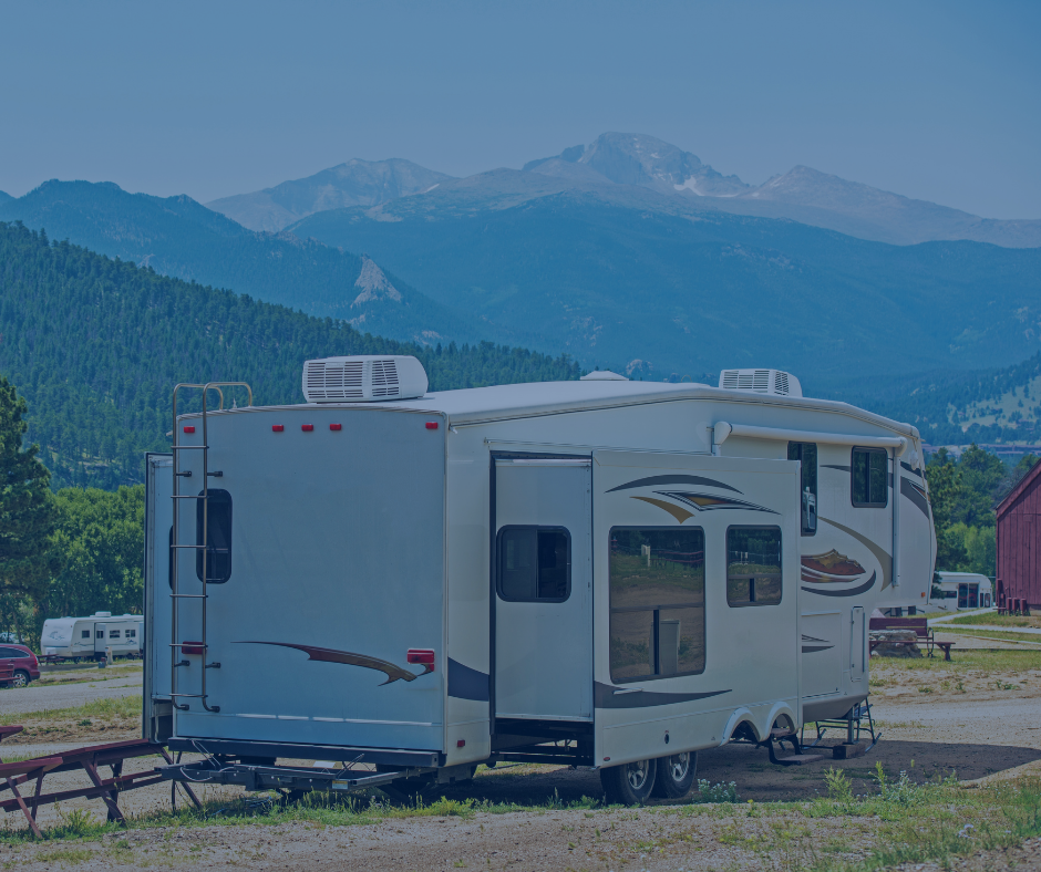 A rv is parked in a field with mountains in the background.