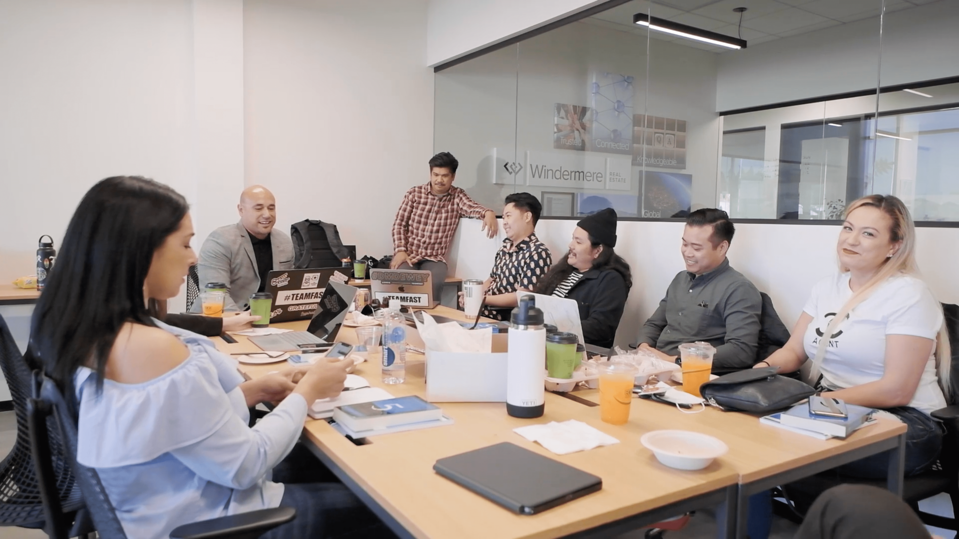 People in a conference room seated around a table, discussing documents and laptops