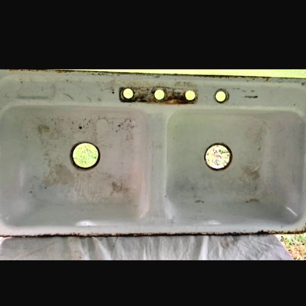 Weathered double basin sink with four faucet holes and circular drain openings, seen from above.