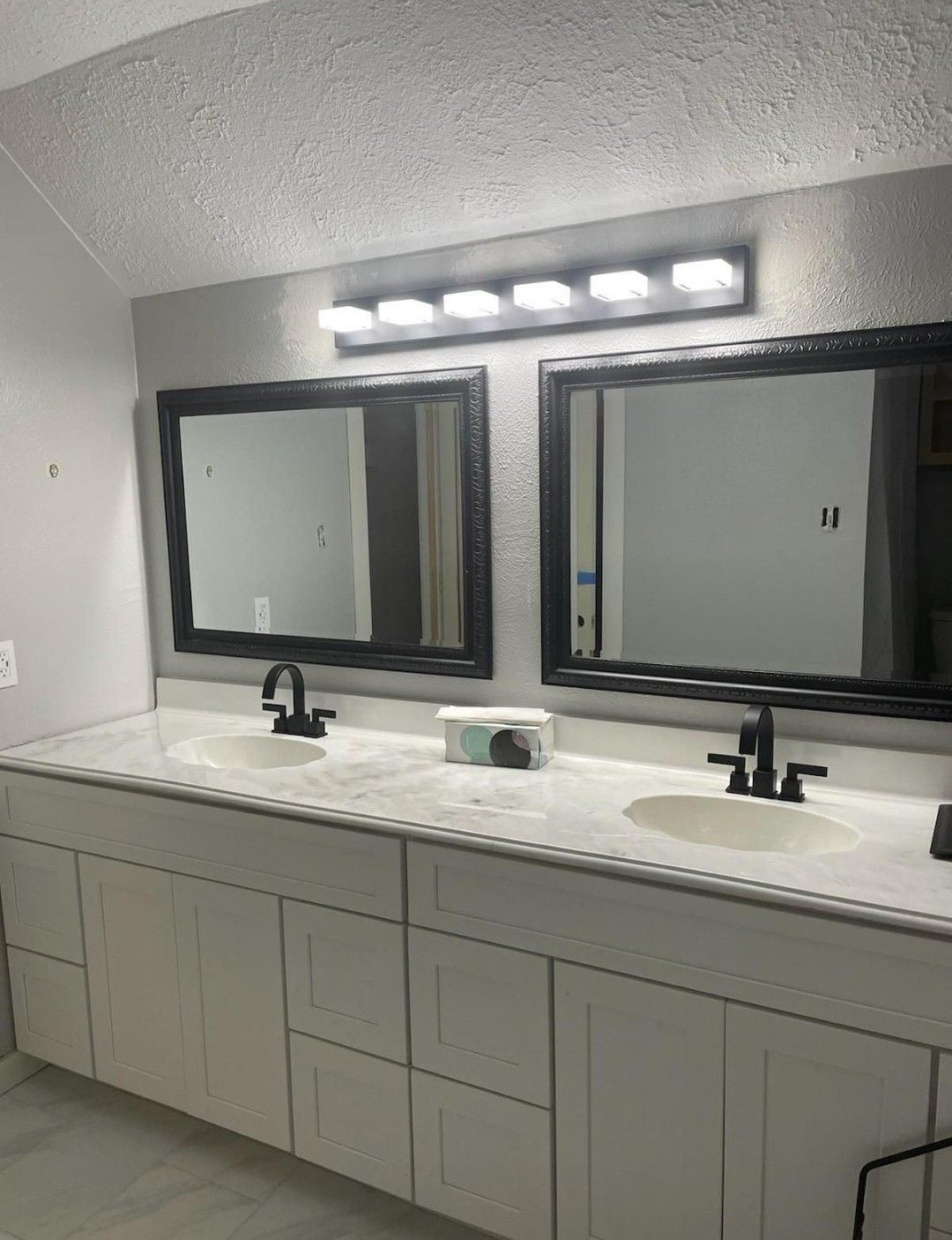 Double bathroom vanity with two mirrors, black faucets, and overhead lights