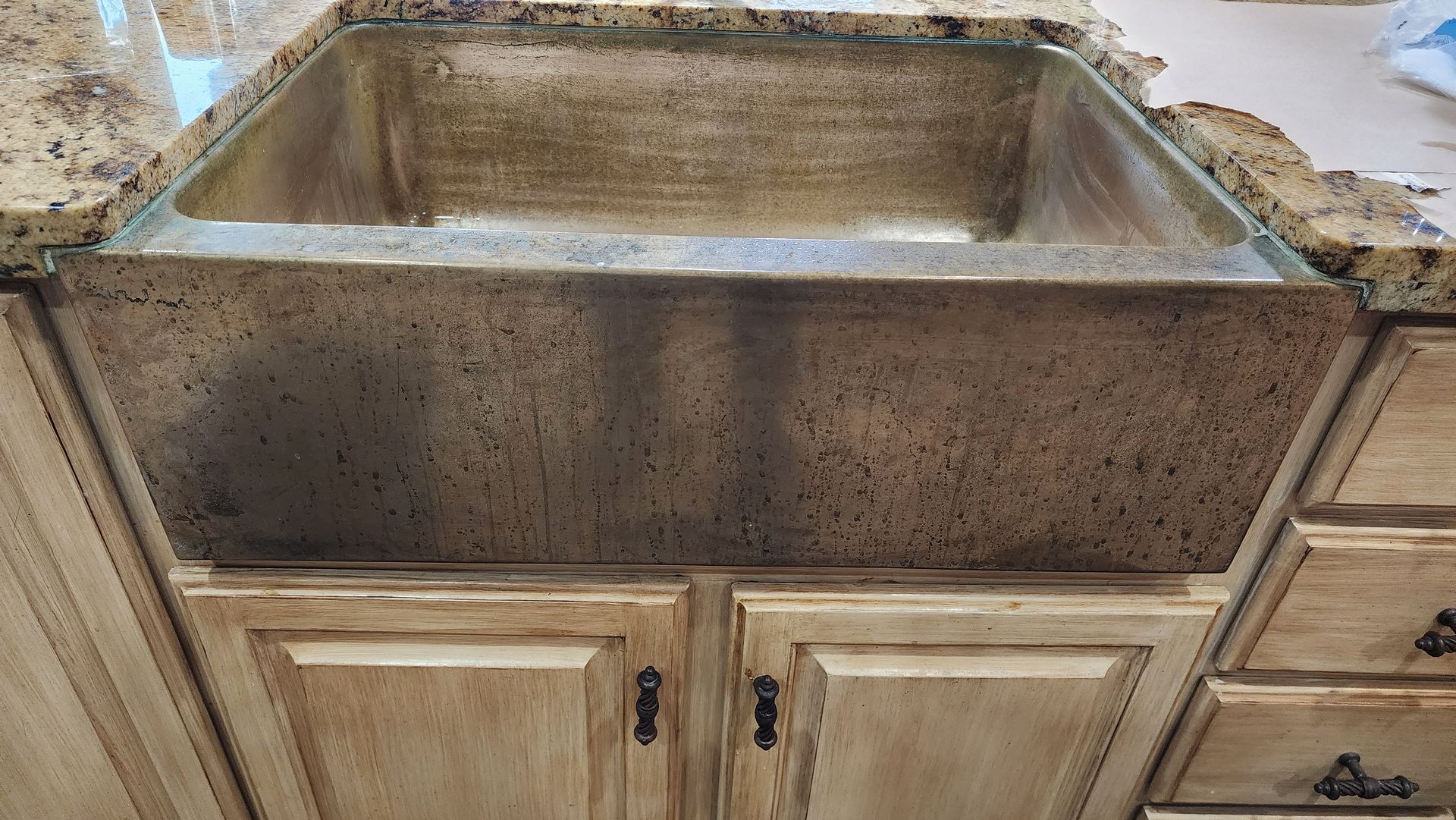 Large granite farmhouse sink set into a light wood kitchen cabinet with drawers on the right.