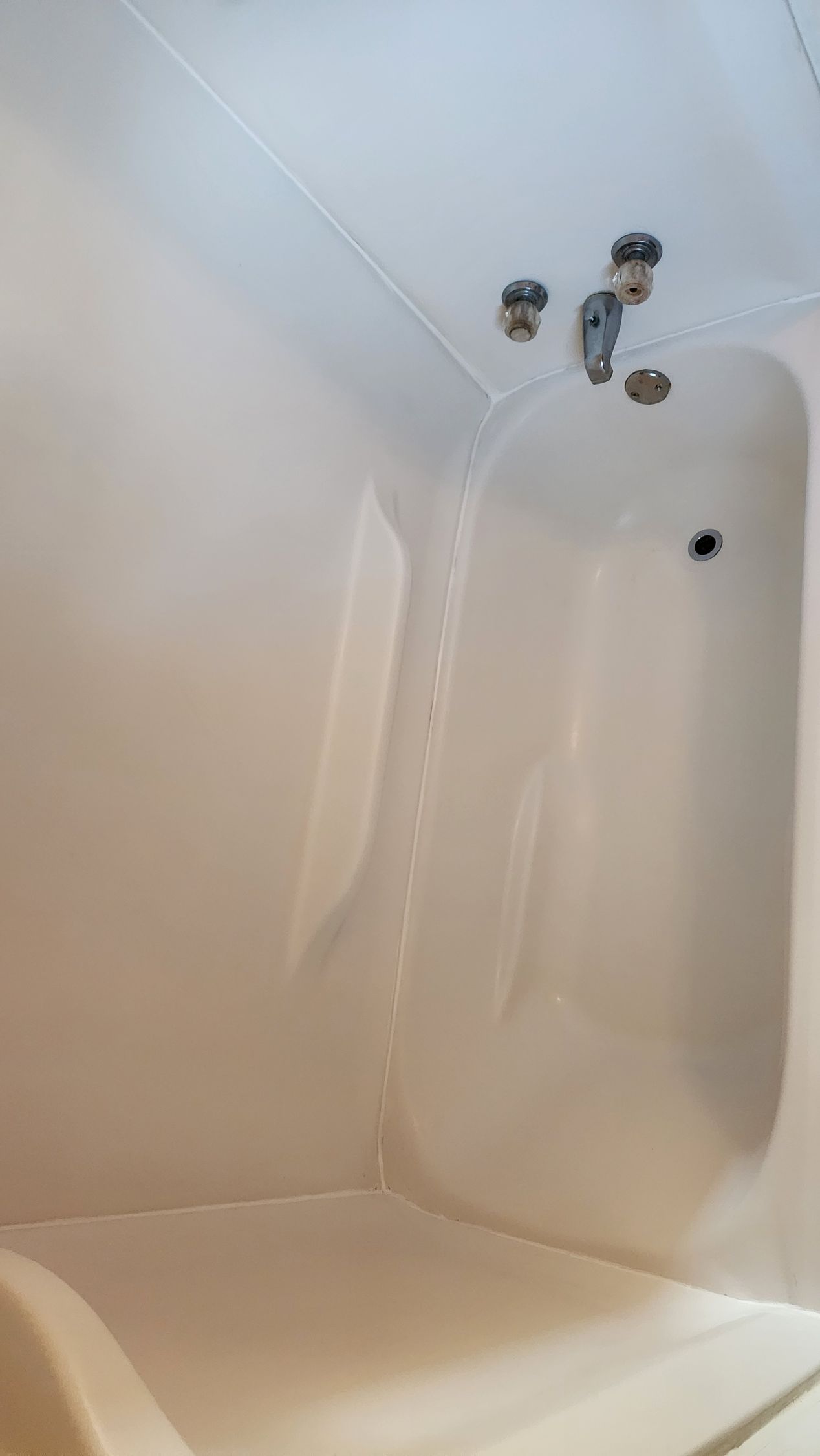 Empty white bathtub with faucet fixtures and a drain hole near the top end